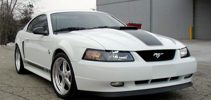 We didn't want anyone to think our white ’04 Mach-1 took a back seat to the acquisition and flogging of our ’05 GT this past season of 2005. Although for the most part our ’05 GT was in the spot light at our shop for the better part of the ’05 season, especially once the Vortech went on.&#10;The Mach-1 did see some minor tweaks, and did make it to the drag strip four times in the ‘05 season. The RWHP was in the high 500’s approaching 600 RWHP and never beat its respectable best of a 10.58 in the 1⁄4 on the 315/35/17 drag radials.&#10;Although In late 2005 the Mach-1 did get a major cosmetic update.&#10;The white ‘04 Mach-1 now sports a new wheel on all four corners that is 18” in diameter and are 9” wide up front and a jaw dropping 11.5” in the rear. The rear tire is now a huge 345/30/18 BF Goodrich drag radial that is meant for the Dodge Viper. This new rear tire is about 12.5” wide, and with the right amount of inner wheel well messaging, modifying, and a couple of 1⁄4” spacers at the wheel hubs, we got them to fit in the rear with a very appropriate look without sticking out too far past the outer wheel lip. It is truly breath taking to see this wide of a non “slick” type tire tucked in the rear of the Mach-1. I've always wanted to put 18” wheels on this car. I feel that the 94 and up body style Mustangs really lends its self and looks the most filled out when they're sporting an 18” rim.&#10;￼&#10;As much as I appreciated the stock Mach-1 wheels and really wanted to keep it looking like a Mach-1 - the fact that the stock wheels were seventeens wasn't doing it for me any more. The rear tires that were formally in the rear were on widened stock wheels that were 10.5” wide and had a BF Goodrich drag radial that was 315/35/17 that looked very tough and filled out from behind, and hooked the car quite well. But the problem I had that most didn't see or care about is that the 315/35/17’s in the rear were actually about 1/4” shorter then the stock 245/45/17’s in the front. And although the ride height was adjusted, it still wasn't quite what I really thought it should look like.&#10;￼&#10;The new rim is a “Hot Wheels” brand wheel and the model I have on the Mach-1 is called the ”68”. As soon as I laid eyes on this wheel, I knew that it had just the right amount of modern styling with a retro look that made it a completely suitable replacement for the Mach-1, and putting it into an 18” rim is really what I wanted in the first place.&#10;The front rims once again are 18X9 with a 275/35/18 BF Goodrich tire and the rear rims were widened to 11.5”, the rear tire is a BFG Drag Radial that measures 345/30/18. This new rim and tire package has renewed the look of the Mach-1, truly brought it up to date and nicely filled it out when you look at it from any angle. And best of all the new rear tire isn't shorter then the front tire, its about 3/8” taller then the new front tire, giving it that tougher, slightly raked stance that I really wanted.&#10;Under The Hood As far as what is going be new or is new for the Mach-1 under the hood for 2006 - It now has a Methanol injection kit that is installed the way most guys don't install them when used on a roots or screw-type blower application. This past summer of 2005 we already learned that Methanol injection is the most effective when its injected into the hot, boosted side of the blower, like into the discharge tube of a Vortech application between the blower and the throttle body. When injected directly into the boosted, hot air, the Methanol can have its greatest effect in lowering the inlet temps a large amount.&#10;We learned that when injecting the Methanol into the inlet of the blower or before the blower like 03-04 Cobra guys or any one with a screw type blower like Kenne Belle’s or Whipple - the Methanol's effectiveness is greatly reduced. We found that instead of lowering the temps as much as 100+ degrees, it can only lower it about 40-60 degrees when injecting the Methanol before the blower. Our only and logical explanation for this is the Methanol is simply being heated up as it comes in contact with the blower’s internal’s. Even still though, you do get the benefit of higher octane and the inlet temps are reduced enough to be justified. &#10;￼&#10;Our shop has tuned two 99 Cobras this past summer that had non-intercooled 1.5-Litre K.B. blowers on them making over 11 psi of boost which is strongly NOT recommended because of excessive inlet temps that are generated by the screw blowers when non intercooled at this boost level. We got them to run exceptional and made from 440 to 465 RWHP on stock “Long Blocks”. These are some pretty good numbers for a non-intercooled KB set up on a 32V 4.6L.&#10;On the Mach though, we removed the entire blower package and lower intake, and proceeded to install a dual nozzle Methanol system that will inject the Methanol were it seems to be the most effective - after the blower/intercooler. My intentions are to step up the tune a little with the Methanol and see if it will make a reliable 635-650 RWHP for the '06 Season and run mid to low tens in the quarter mile when the outside temp is over 85 degrees, and not only run great 1⁄4 mile numbers when its cool/cold outside. This will be our first experience with a Methanol kit installed after the blower on a roots/screw blower application.&#10;￼&#10;Also on the Mach-1, the rest of the Methanol kit was installed in a bit more serious nature as well. The battery was tastefully relocated into the trunk in the spare tire “well”, under the trunk mat. And Vortech’s larger intercooler reservoir was used where the battery once went to house almost two gallons of Methanol. The Vortech reservoir is designed to 100% neatly bolt into where the battery would normally go. And as mentioned a paragraph ago, the Methanol injector jets are located at the bottom of the lower intake putting the Methanol into the intake stream after the blower. We will not have any performance updates with the Methanol until Spring 2006.&#10;&#10;